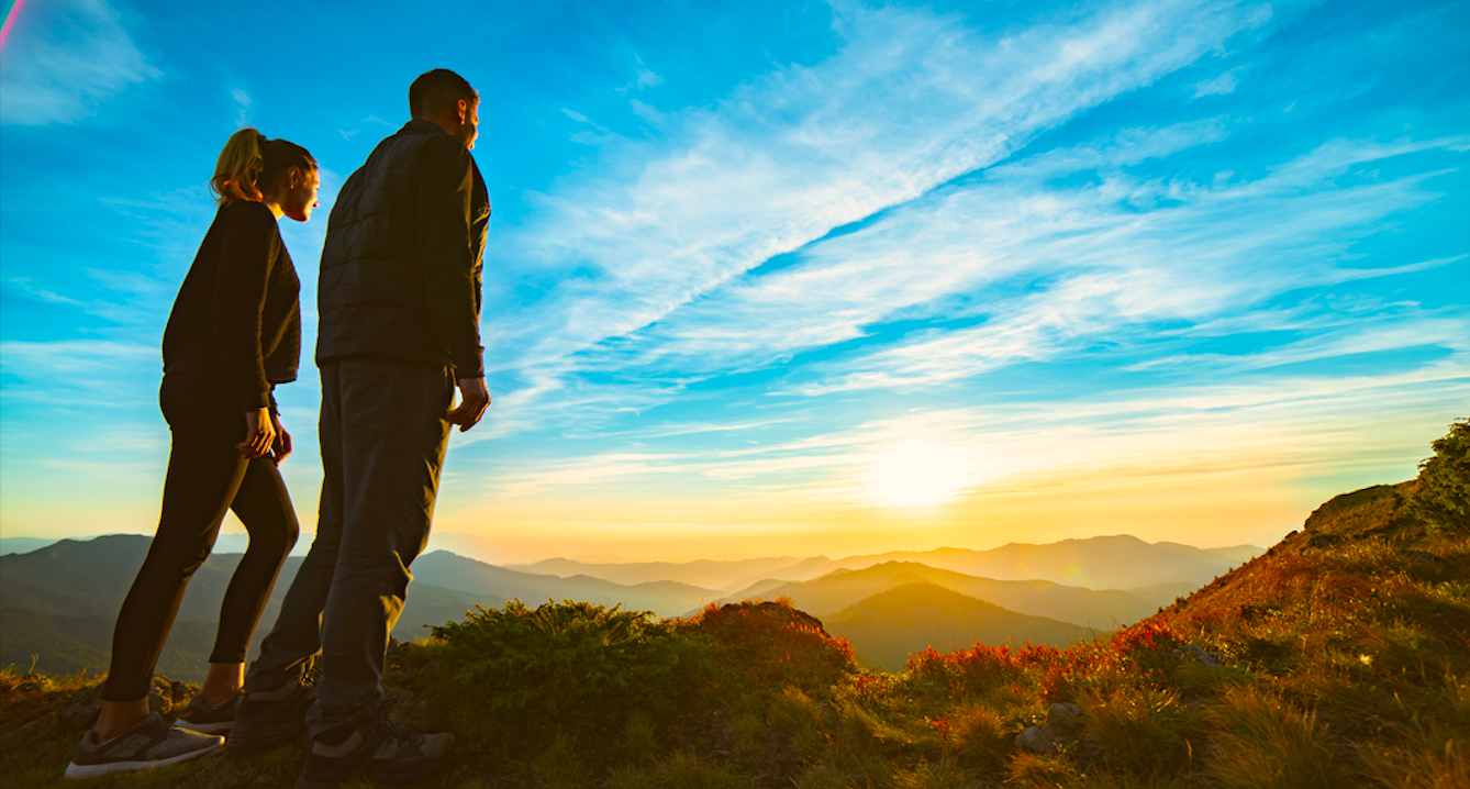 Un couple, auteur de leur vie, atteignet le sommet de la montagne et admirent le soleil qui se lève sur un jour heureux.